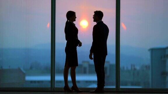 在明亮的阳光背景下一对生意上的夫妇在窗前交谈