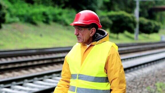 身穿黄色制服的铁路工人站在铁轨上抽烟