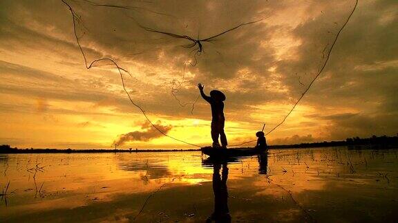 清晨日出前亚洲渔民在木船上撒网捕鱼