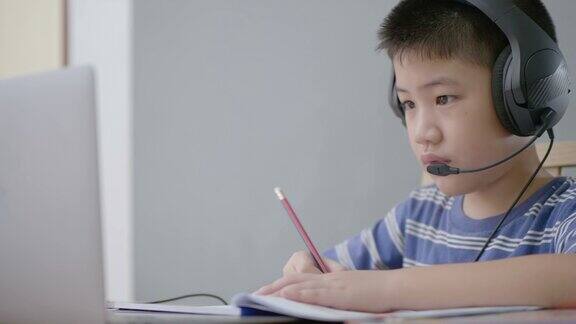 新常态亚洲男孩学习在线看着屏幕笔记本电脑在家里专心写作技术教育