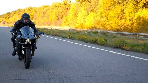一个戴着头盔的年轻人在秋天的高速公路上骑着现代摩托车飞驰摩托车手开着前灯在乡村公路上比赛一个家伙在旅行中骑自行车自由