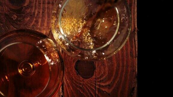 豪华白兰地手把金色的干邑白兰地从一个圆瓶里倒进一个棕色木桌上的玻璃杯里旁边是一个黑色背景的玻璃杯白兰地干邑嗅酒狂欢