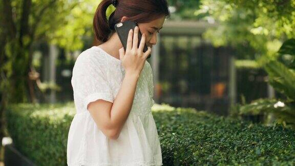 在花园里一位东南亚美女正在用智能手机和朋友聊天