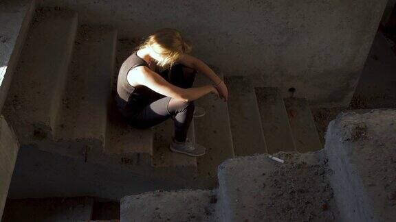 一个不整洁的女孩正坐在一幢废弃建筑的楼梯前