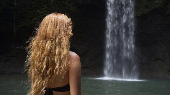 年轻女子穿着比基尼站在水里欣赏瀑布