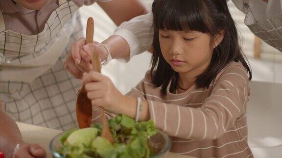 快乐快乐的亚洲家庭母亲父亲和可爱的小女孩一起在厨房烹饪沙拉的时间