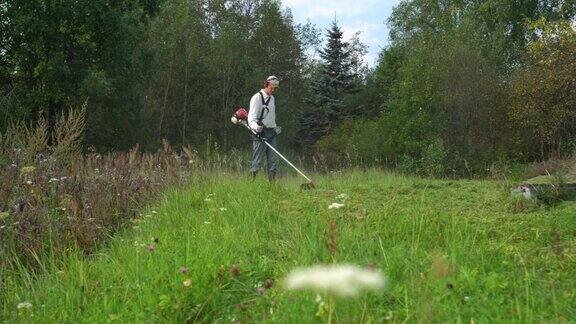 一名男子用手动汽油割草机割高野草园丁割草机照料野生花园的绿草园艺治疗
