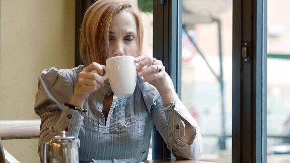 在靠窗的自助餐厅喝热茶:沉思的女人端着一杯茶
