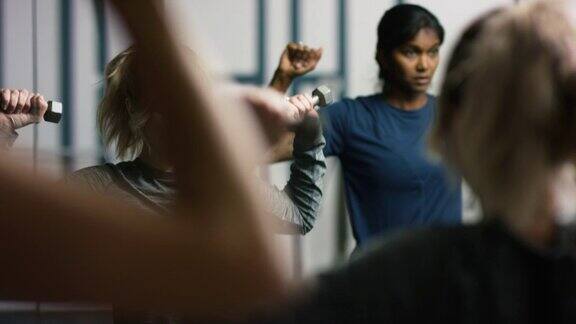 一个白种人女人和一个亚洲印度女人(都在他们的二十多岁)在健身房用手做肩部练习