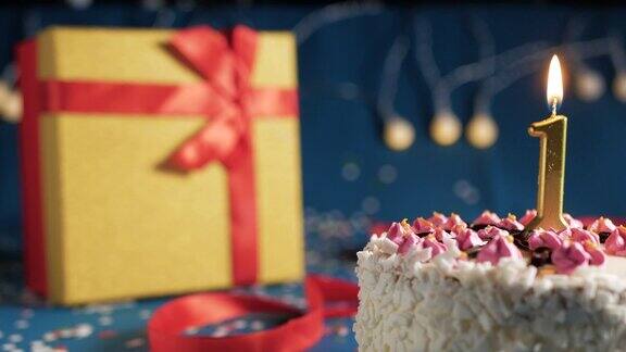 白色生日蛋糕1号金色蜡烛用打火机点燃蓝色背景用彩灯和礼物黄色盒子用红丝带绑起来特写镜头