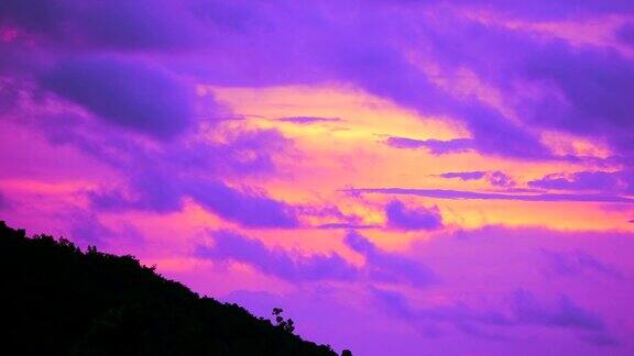 日落天空与紫色的云移过绿色的山顶剪影山