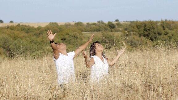 祈祷一个穿着白衣的男人和一个女人站在草地上伸开双臂