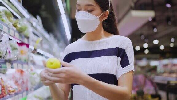 年轻的成年亚洲女性戴着防护口罩在百货商场精心挑选新鲜产品或消费产品欢快的新常态购物生活方式