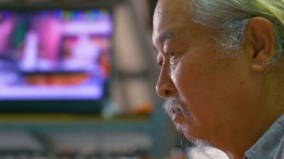肖像的亚洲老人白发看电视和吃早餐