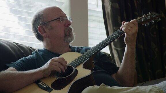一名五十多岁的白人男子在客厅里弹原声吉他