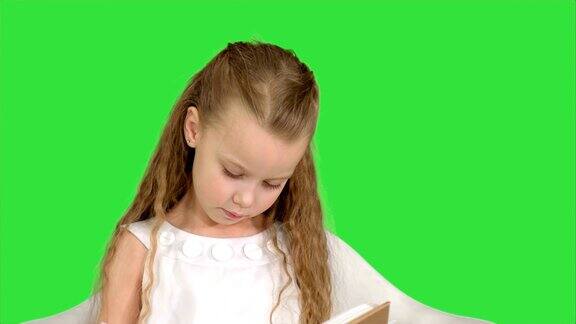 漂亮的小女孩坐在书和阅读在绿色屏幕上色度键