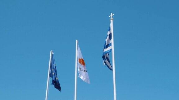 旗杆上的希腊、塞浦路斯和欧盟的旗帜迎风飘扬映衬着湛蓝的天空