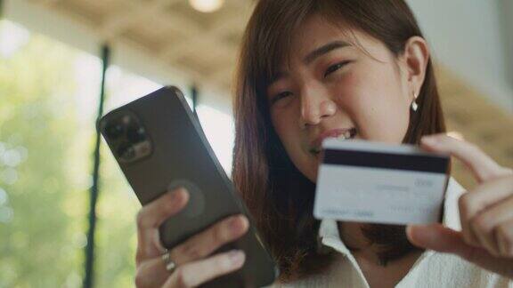 年轻的亚洲女性用信用卡在手机上在线订购