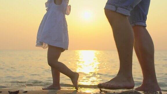 小婴儿学走路第一个步骤慢镜头120帧父亲正在教他孩子小女孩在夏天的沙滩上做沙滩上的第一步宝宝的脚快乐的童年幸福的家庭近距离观察脚