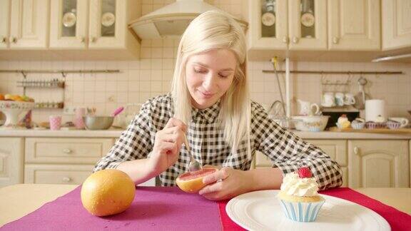 年轻的金发女郎在健康和不健康的食物之间做选择柚子和美味的松饼在她对面的桌子上