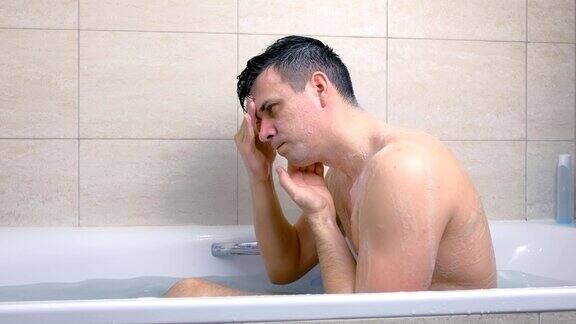 男人坐在浴缸里洗脸用按摩动作把磨砂膏抹在脸上