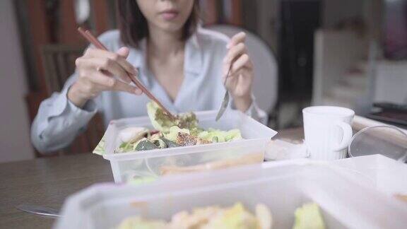 亚洲女性在家中用餐餐桌上一次性饭盒使用筷子和勺子食品外卖服务应用蔬菜沙拉饮食营养外卖食品新常态
