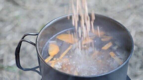 在火上把谷物加入沸水中烹饪对自然在燃烧的炉子上准备野营食物旅游营的游客烹饪