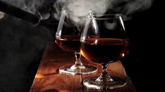 豪华白兰地棕色的木桌上放着两杯金色的白兰地背景是黑色一个在抽雪茄的男人冒烟了白兰地干邑嗅酒狂欢
