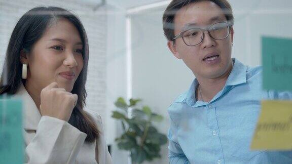 两个亚洲商人看着玻璃白板头脑风暴讨论分享商业想法一起工作