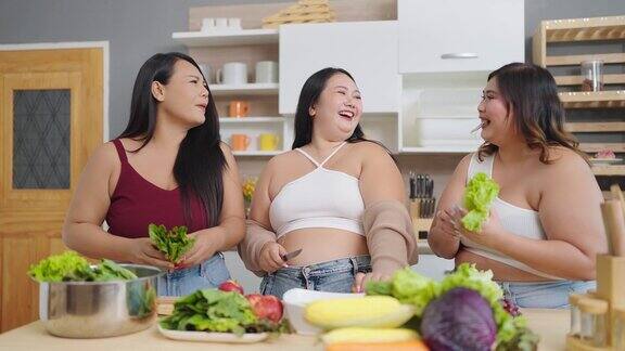 一群快乐的胖乎乎的女性朋友一起做饭准备沙拉三个亚洲大码女人在厨房里聊天做沙拉健康食物概念