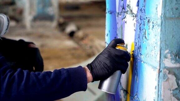 特写镜头中一只戴着防护手套的男性手拿着喷雾剂涂料在废弃建筑内的柱子上涂鸦现代艺术抽象形象和人的观念