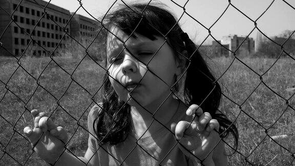 一个伤心的孩子躲在篱笆后面