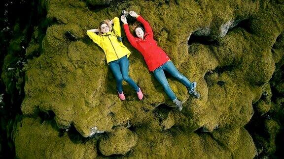 两名女子徒步旅行后躺在冰岛熔岩上休息的鸟瞰图直升机转过来快乐的雌性