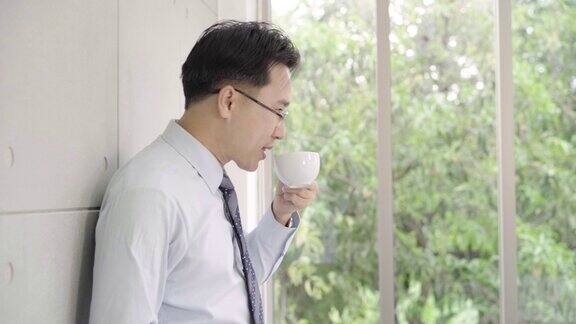 慢镜头一个成熟的亚洲商人一边喝着咖啡一边从一幢写字楼里望着窗外的城市