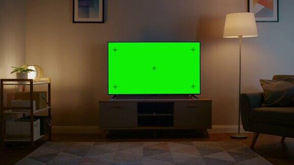 放大镜头与水平绿色屏幕模拟电视舒适的夜晚客厅家里有一把椅子和打开的灯