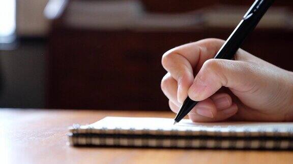 一个女人的手写在木桌上的空白笔记本上的慢动作