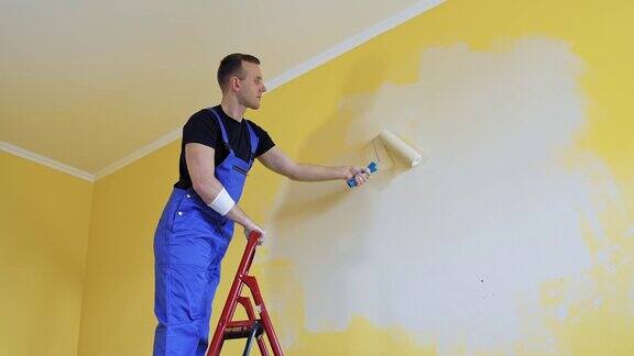 工人从梯子上重新粉刷公寓的墙壁年轻的建筑工人男性装饰墙壁成为新的浅色回家修理
