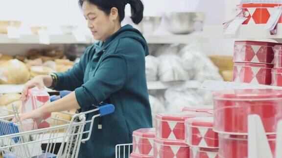 亚洲妇女从货架上拿红色的盒子到购物推车为圣诞礼物在百货公司新年假期