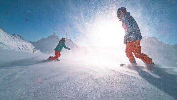 SLOMOTS男性和女性滑雪板骑下一个阳光斜坡和雪颗粒在空中飞行
