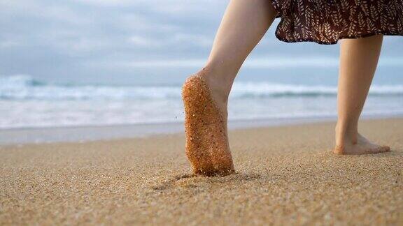 女孩的双腿走在大海潮湿的沙滩上留下脚印