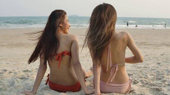 两个女孩坐在海滩上的后视图两个亚洲女人在海边休息缓慢的运动