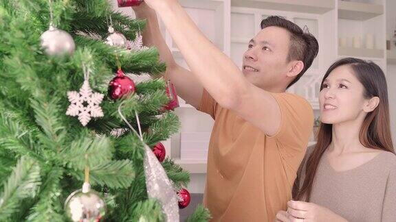 圣诞节期间亚洲夫妇在家里的客厅里装饰圣诞树心情愉快生活方式女人和男人快乐庆祝夏天圣诞节和新年