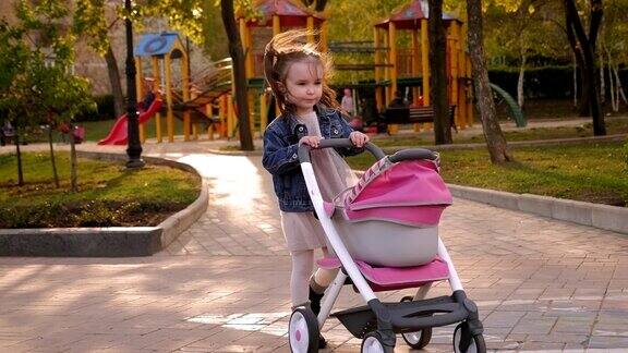 操场上的公园里一个小女孩推着一辆婴儿车在她前面