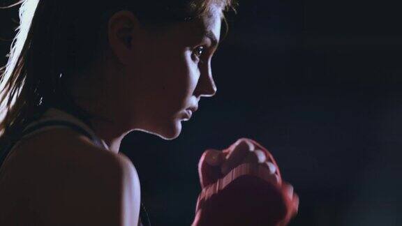 一位美丽的女拳击手在黑暗的健身房里训练用慢动作练习出拳相机运动侧视图替身拍摄
