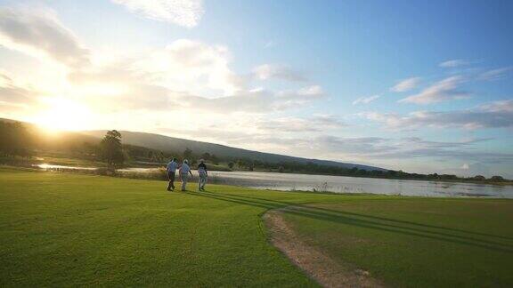 在夏日夕阳下一群亚洲男子高尔夫球手在高尔夫球场边散步边交谈