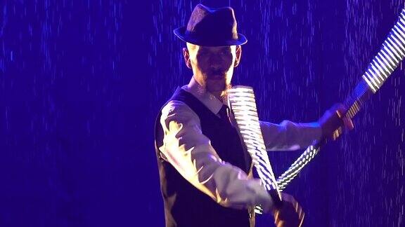 在蓝色灯光和烟雾的背景下一个时尚男子的剪影用发光的LED棒表演在一个黑暗的演播室里一个男人在雨点间展示了一场篝火表演用慢动作拉近镜头