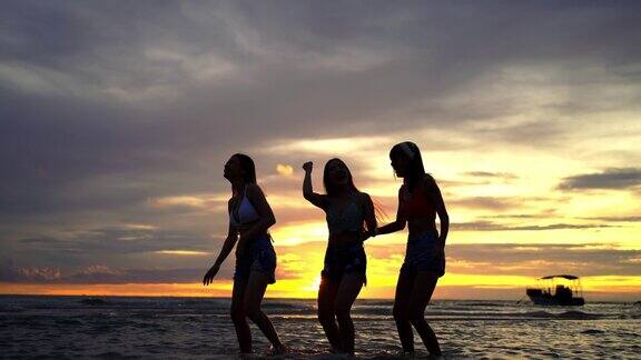 4K剪影一群亚洲女子在夏日夕阳下的热带海岛海滩上跳舞