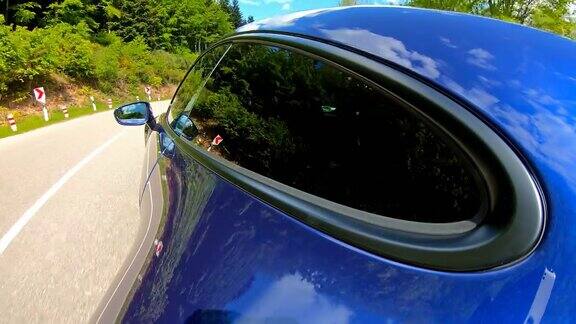 在一个阳光明媚的日子里驾驶着一辆优雅豪华的蓝色跑车行驶在风景如画的道路上