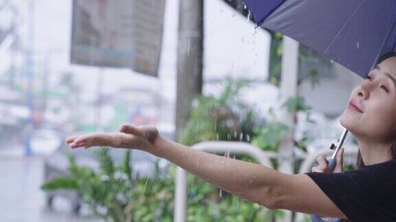 年轻的亚洲女性拿着雨伞坐在路边等着大雨滂沱暴雨暴雨的季节她伸出手触摸雨滴卡在雨中正好奇的脸