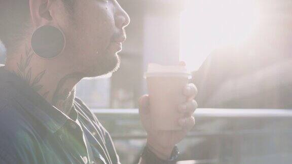一个年轻的亚洲男人在城市里用智能手机拿着咖啡杯